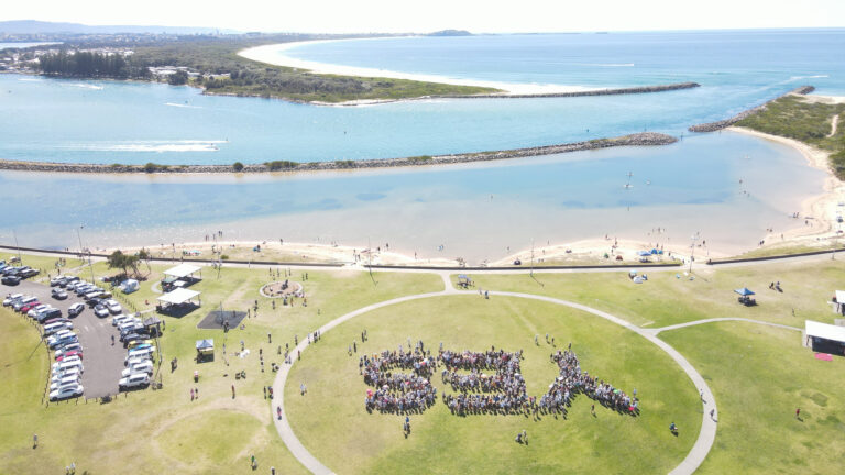 Aerial view of coastal park event with crowd forming yes inside circle