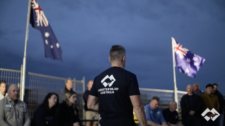 Disaster Relief Australia team briefing outdoors with flags at dusk