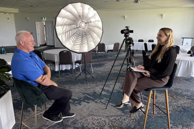Woman interviewing man with studio light and tripod camera in event hall