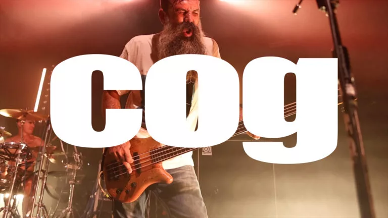 Bass guitarist performing live with drummer on stage under warm orange lighting